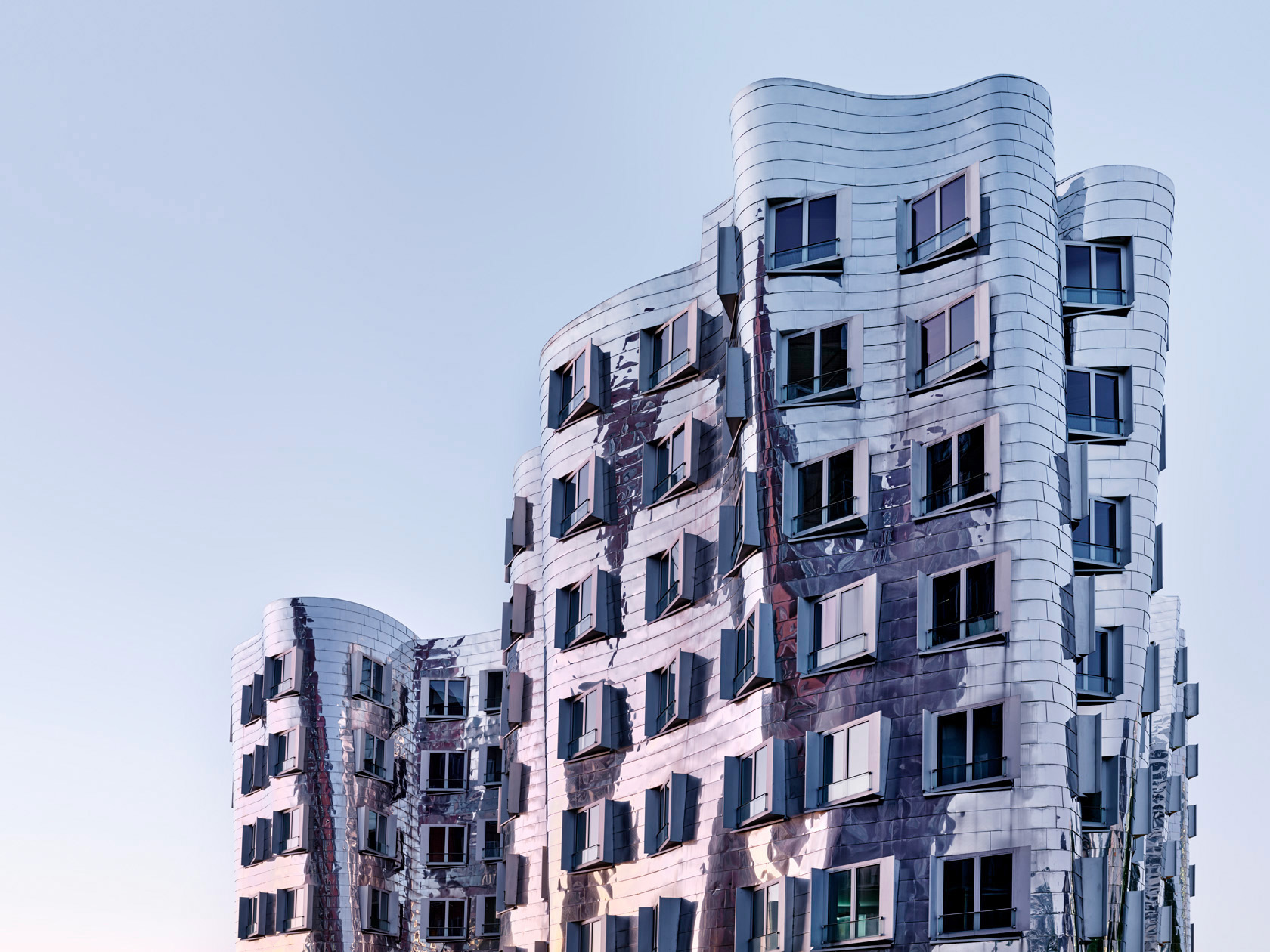 Die Fotografie Zollhof von Herbert Böttcher zeigt eine geschwungene, reflektierende Metallfassade eines modernen Gebäudes vom Architekten Frank O. Gehry im Medienhafen Düsseldorf.