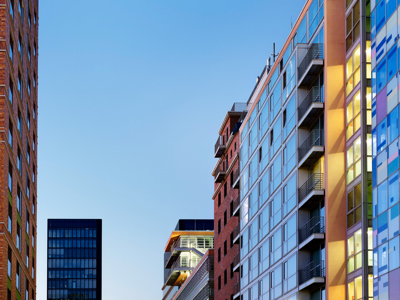 Die Fotografie von Herbert Böttcher zeigt den Blick von der Speditionsstrasse im Medienhafen Düsseldorf auf moderne Stadtgebäude mit Glasfassaden und Backsteinarchitektur bei klarem Abendhimmel.