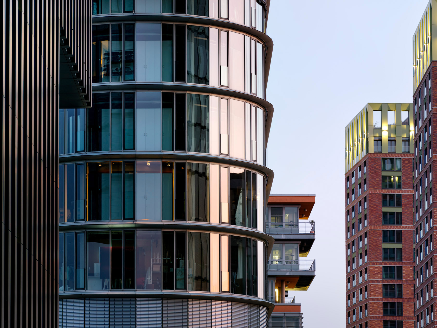 Die Aufnahme des Fotografen Herbert Böttcher zeigt einen markanten Ausschnitt der modernen Architektur im Düsseldorfer Medienhafen. Im Fokus des ausgewählten Bereichs steht die gläserne, geschwungene Fassade eines der Türme der Hafenspitze und dem Hochhaus Win Win auf der rechten Seite.