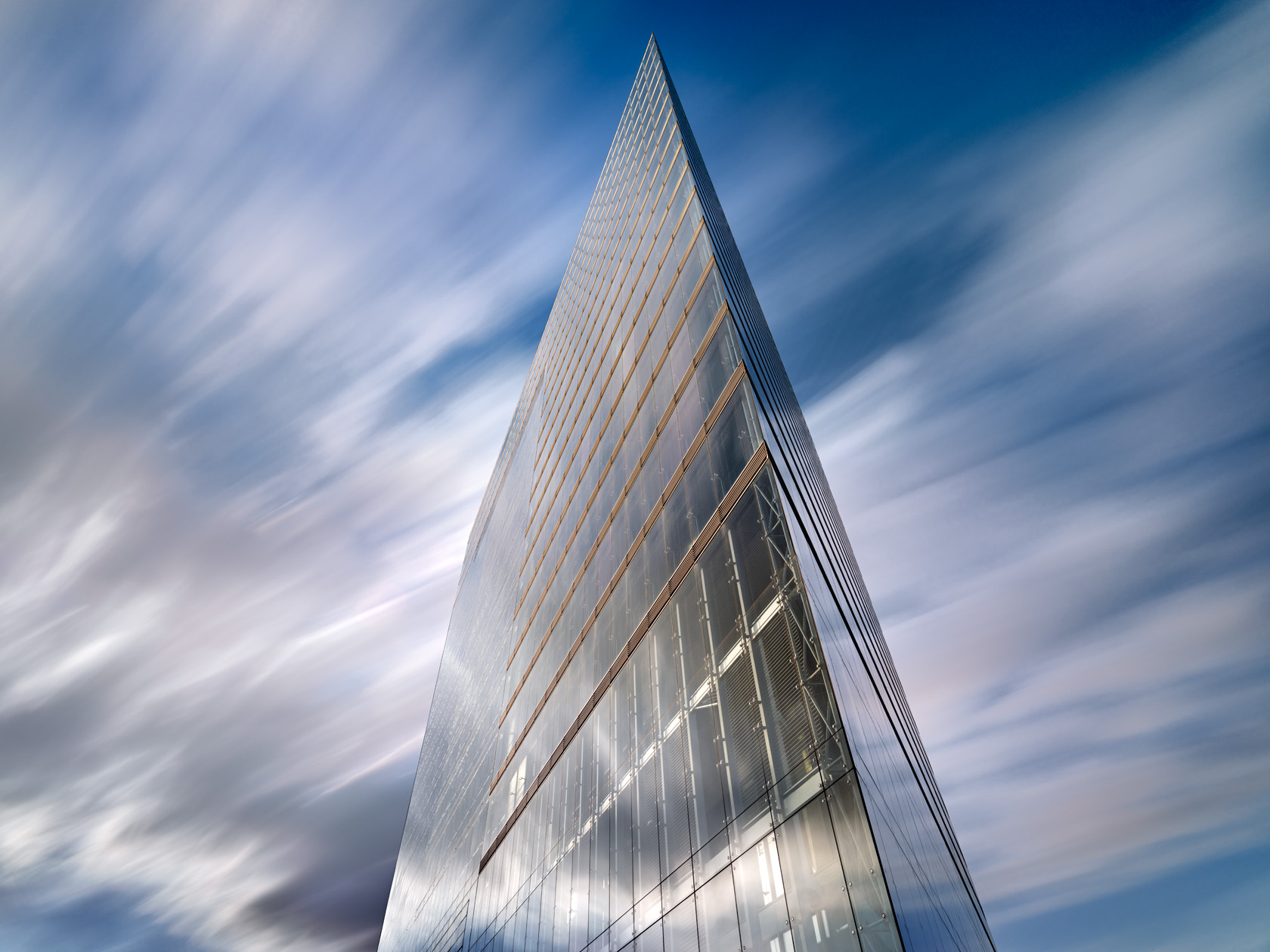 Untersicht des Düsseldorfer Stadttors mit moderner Glasfassade vor dynamischem Wolkenhimmel, Architekturfotografie von Herbert Böttcher.