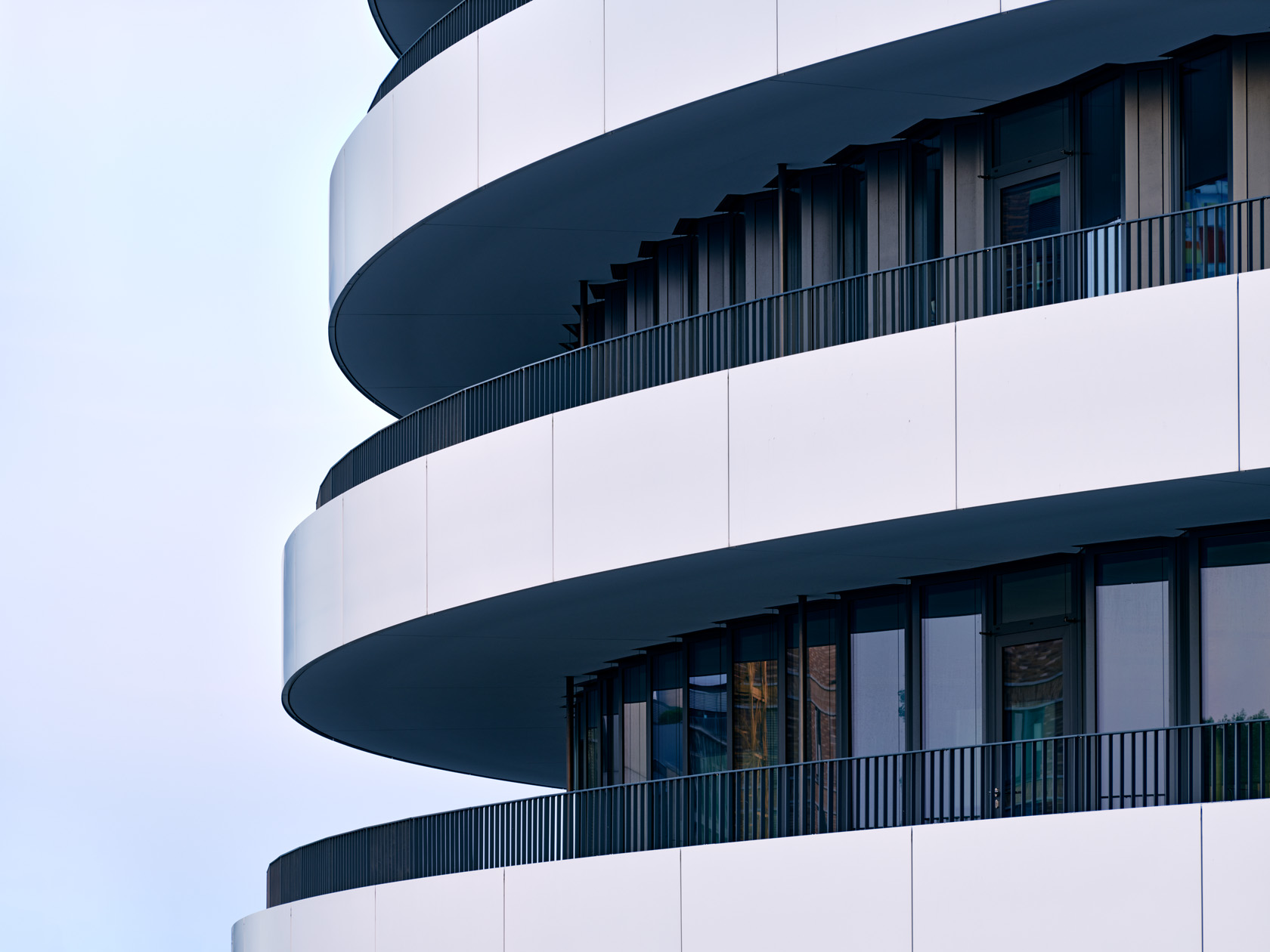 Die Fotografie von Herbert Böttcher zeigt die geschwungene, weiße Fassade des Trivago Campus im Düsseldorfer Medienhafen vor blauem Himmel.