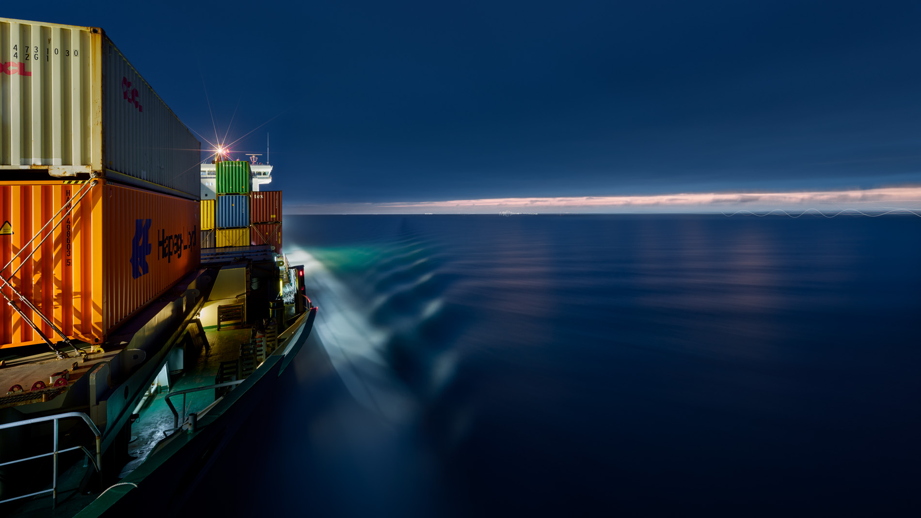 Sie sehen das miSie sehen das mit Containern beladene beleuchtete Vorschiff des Containerschiffs Elbsun mit Blickrichtung zum Steuerhaus während der Fahrt in der blauen Dämmerung. Durch die Langzeitbelichtung wirkt die Oberfläche des Wassers geglättet. Containern beladene beleuchtete Vorschiff des Containerschiffs Elbsun mit Blickrichtung zum Steuerhaus während der Fahrt in der Dämmerung. Durch die Langzeitbelichtung wirkt die Oberfläche des Wassers geglättet.