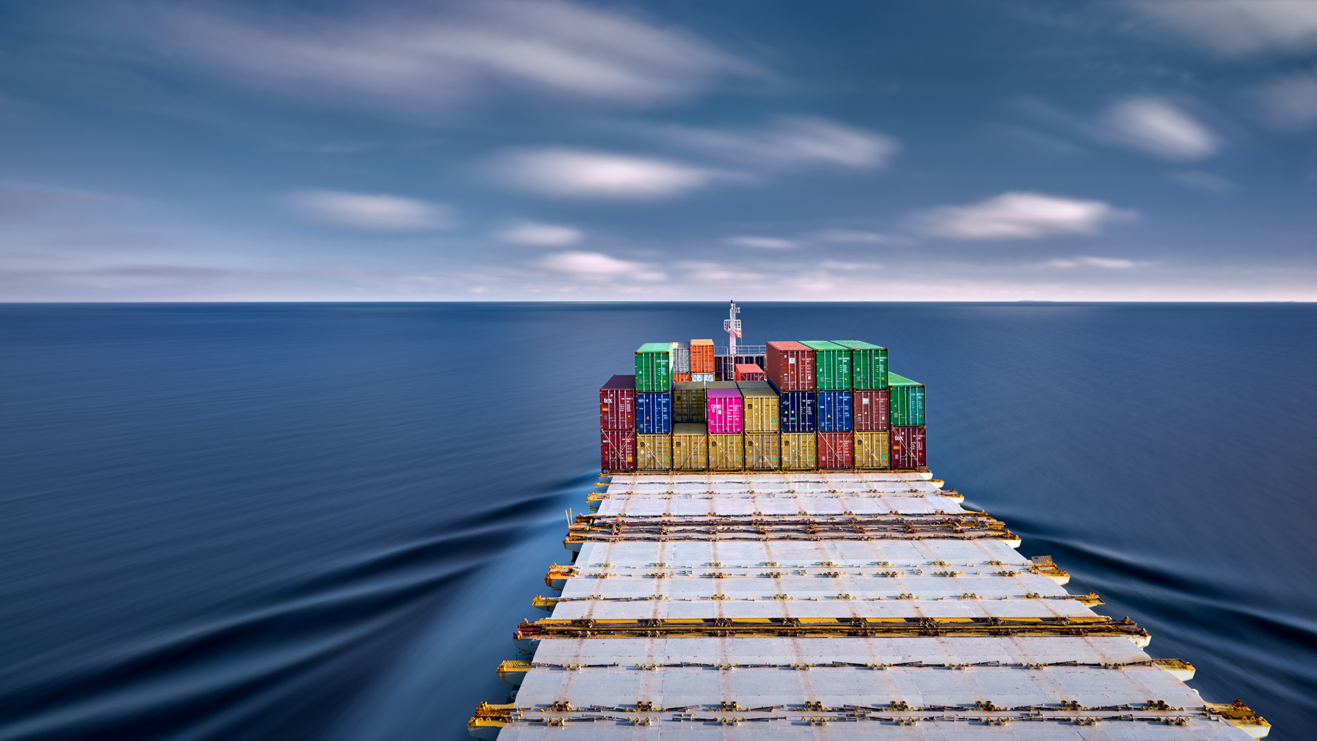 Ein mit Containern beladenes und teilweise leeres Vorschiff des Containerschiffs Elbsun während der Fahrt bei blauem Himmel und schnell ziehenden weißen Wolken. Durch die Langzeitbelichtung wirkt die Oberfläche des Wassers geglättet.
