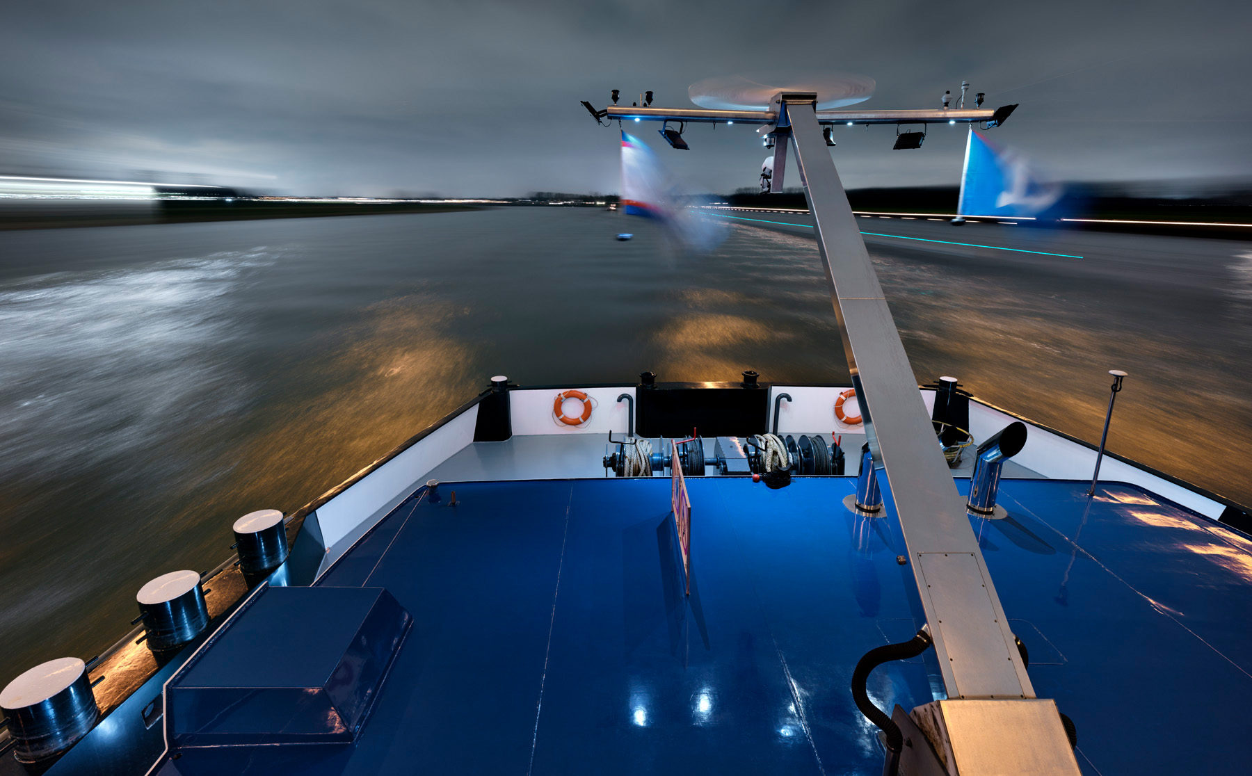 Die Fotografie von Herbert Böttcher zeigt den Bug eines modernen Binnenschiffs der Reederei Deymann während der Fahrt auf einer Wasserstasse bei Nacht.